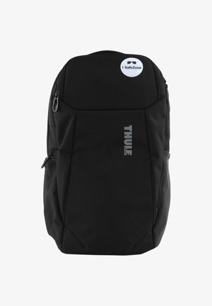 Un sac à dos noir avec une finition texturée, présentant un logo THULE bien en vue. Comprend une étiquette SafeZone circulaire et des poches zippées.