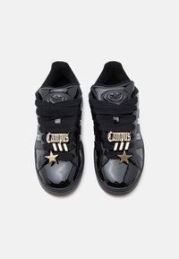 Μαύρα γυαλιστερά sneakers Adidas Campus με παχιά μαύρα κορδόνια, χρυσές ετικέτες "Campus" και διακοσμητικά σε σχήμα αστεριού σε λευκό φόντο.