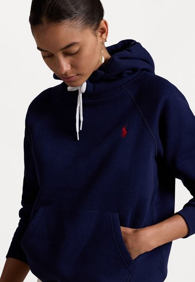 Navy blauwe hoodie gemaakt van zachte stof, met een kangoeroezak, witte trekkoorden en een klein rood logo op de borst.