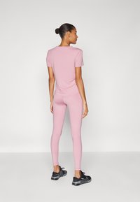 Maglietta rosa a maniche corte con scollo tondo, abbinata a leggings rosa aderenti e scarpe da ginnastica nere con un design testurizzato.