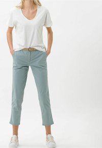 Witte V-hals t-shirt gecombineerd met lichtgroene cropped broek en een tan kleurige riem. Sneakers met witte veters maken de outfit compleet. Eenvoudig ontwerp en pasvorm.