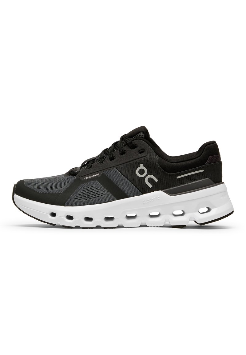 Chaussure de sport noire et grise avec une tige en mesh, une semelle intermédiaire blanche rembourrée avec des sections évidées, et une semelle extérieure en caoutchouc noir.