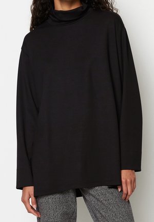 Pull à col roulé noir avec des manches longues et amples. Tissu doux et extensible avec une coupe décontractée, associé à un pantalon à motif pied-de-poule.