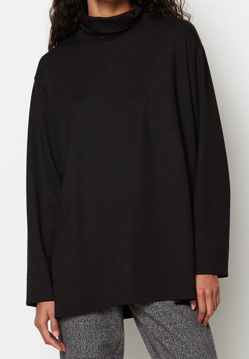 Schwarzer Rollkragenpullover mit langen, lockeren Ärmel. Weicher, dehnbarer Stoff mit legerem Schnitt, kombiniert mit Hahnentrittmuster-Hosen.