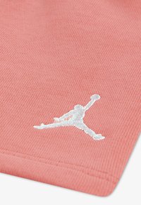 Ύφασμα από βαμβάκι κοραλλί με ριγωτή υφή, στο οποίο υπάρχει λευκό κεντημένο λογότυπο Jumpman που απεικονίζει πόζα καλαθοσφαίρισης στον αέρα.