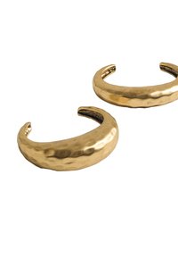 Bransoletki na nadgarstek w kolorze złotym z metalowym, młotkowanym wykończeniem i otwartymi końcami, o gładkiej i zaokrąglonej formie.