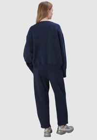 Marineblauwe oversized sweatshirt met verlaagde schouders, geribbelde manchetten en bijpassende losse broek; gedragen met metallic sneakers.