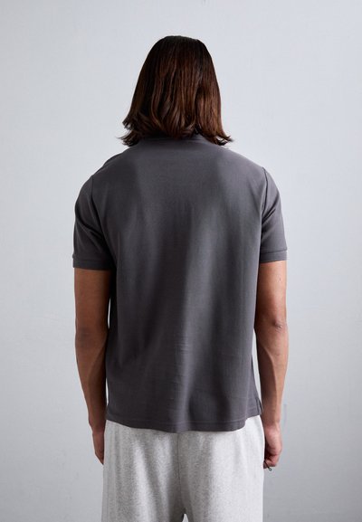Graues Kurzarm-Polohemd mit glatter Textur, ausgestattet mit einem klassischen Kragen und geradem Saum, kombiniert mit hellgrauen Jogginghosen.