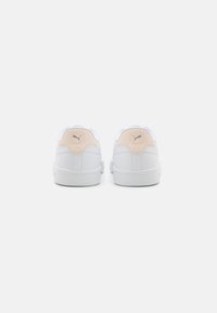 Zapatillas deportivas blancas con un upper de cuero liso, con un acento melocotón en el talón, suela de goma y logo grabado en la parte trasera.