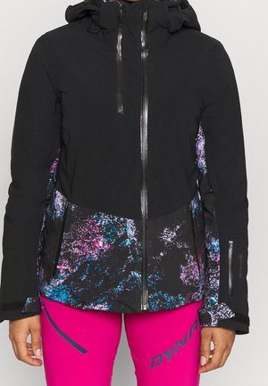 Zwarte capuchonjas met abstract patroon in paars, blauw en roze en felroze broek met "DYNA"-logo op het dijbeen.