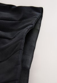 Tissu noir à texture douce, présentant un design froncé et un bord côtelé. Gros plan mettant en valeur les détails du matériau et de la confection.