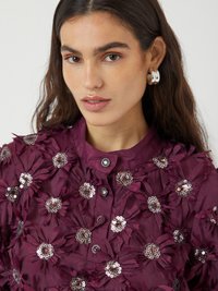 Bordeaux bluse med blomsterapplikasjoner og paljetter, med rund halslinje og knappeåpning. Glatt stoff med teksturerte blomsterdetaljer.