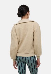 Pull en polaire beige avec un grand col et un ourlet côtelé, associé à des leggings à motifs présentant des designs géométriques verts et marine.