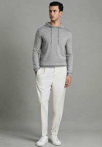 Grauem Baumwollhoodie mit Kordeln, kombiniert mit weißen plissierten Hosen und weißen Sneakers. Schlichter, geradliniger Design.