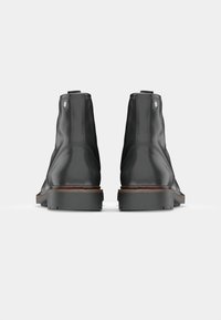 Botas de tobillo de cuero negro con textura suave, punta redondeada y suela de goma. Dos lengüetas en la parte posterior y detalles de costura mínimos.