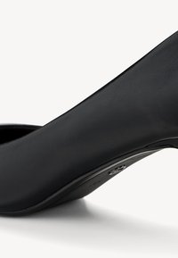 Svart hælsk Shoe laget av glatt lær, med spiss tå og en avsmalnet design med en blank aksent på hælen.