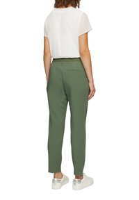 Groene broek met een strakke taille, voorzien van een achterzak. Gecombineerd met een losse witte blouse en witte sneakers met zilveren accenten.
