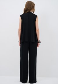 Haut sans manches noir avec un col montant et un design fluide, associé à un pantalon noir ample et long jusqu'au sol. Texture de tissu lisse.