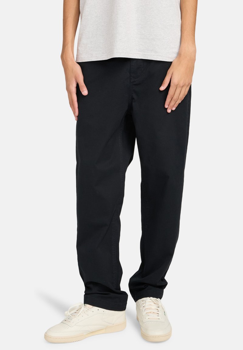 Zwarte katoenen broek met een relaxte pasvorm, rechte pijpen en zijzakken, gedragen met witte sneakers en een lichtgrijze shirt.