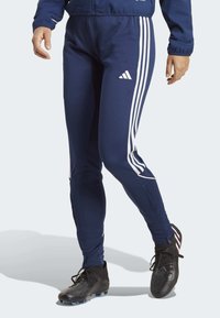 Marine sportbroek met witte drie-stripes aan de zijkanten, een slim fit en een elastische tailleband. Het materiaal lijkt glad en rekbaar.