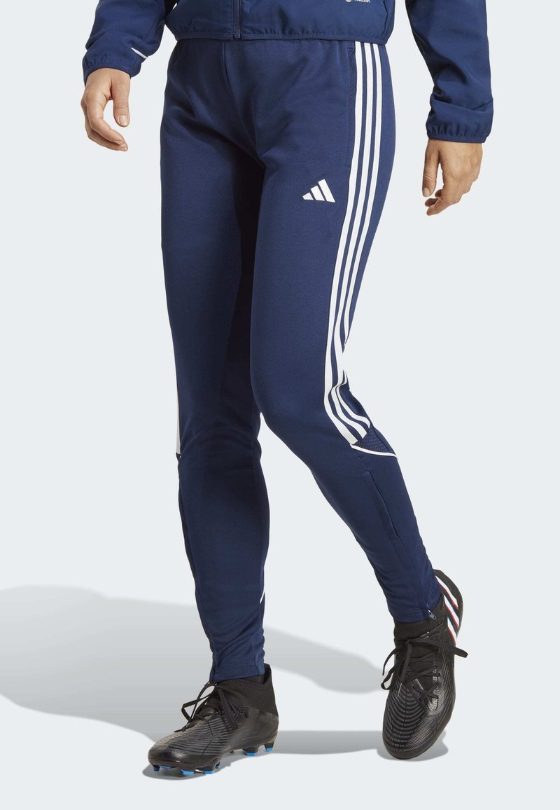 Marine sportbroek met witte drie-stripes aan de zijkanten, een slim fit en een elastische tailleband. Het materiaal lijkt glad en rekbaar.