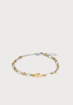 Bracelet chaîne en métal bicolore avec un emblème crocodile doré et une fermeture à mousqueton argentée.