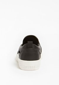 Černé nazouvací boty s hladkým koženým povrchem, bílou gumovou podrážkou a malým smyčkovým úchopem na zadní straně pro snadné obouvání. Na patě mají logo.