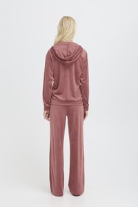 Tuta in velluto rosa pallido, con top con cappuccio e pantaloni a gamba larga. Texture liscia con vestibilità rilassata e maniche lunghe.