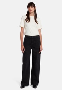Pantaloni cargo neri a gamba larga con due tasche frontali, abbinati a una maglietta a maniche corte color crema. Tessuto liscio con una vestibilità rilassata.