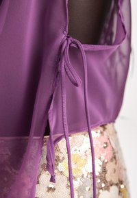 Purple sheer fabric with tie closures near the shoulder, paired with a multicolored sequin skirt featuring various circular patterns.