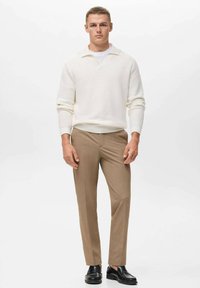 Knit white sweater with a V-neck, paired with light brown tailored pants. Black shoes. Sleek, fitted design with ribbed texture.