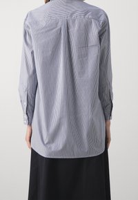 Camicia a maniche lunghe a righe blu e bianche con yoke posteriore e polsini con bottone, caratterizzata da un orlo dritto e una superficie tessuta liscia.