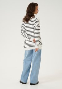 Haut à rayures à manches longues en blanc et noir avec une coupe décontractée, associé à un jean large bleu clair et des chaussures noires. Tissu au toucher lisse.