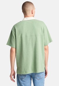 Grön kortärmad skjorta med vit krage, avslappnad passform, bomullsmaterial, enfärgad och en sömdetalj över ryggen.