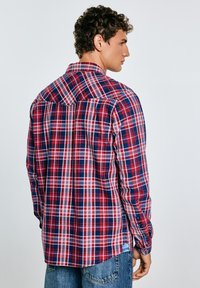 Rød og navy ternet flannel skjorte med lange ærmer, knapmanchetter og en buet kant. Har et yoke-design på ryggen. Tekstureret stof.