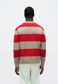 Rdeč in bež pulover z dolgimi rokavi, okroglim izrezom, rebrasto strukturo in detajlom šivanja v obliki črke V na hrbtni strani.