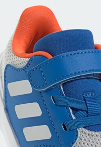 Niebieski but sportowy z teksturowaną, szarą siateczkową cholewką, pomarańczową wyściółką, trzema odblaskowymi srebrnymi paskami i rzepem.