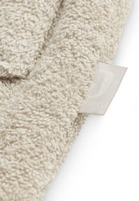 Serviette texturée beige avec une surface duveteuse. Présente un bord droit et une petite étiquette tissée dans le coin. Tissu doux et absorbant.