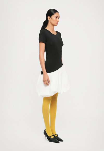 Zwarte getailleerde top, witte poffende rok, gele panty en zwarte hoge hakken. Glad materiaal met contrasterende kleuren en eenvoudig ontwerp.