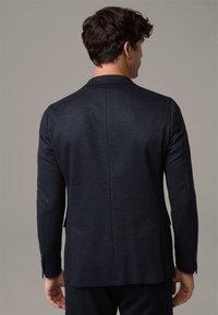 Granatowa marynarka wykonana z teksturowanej tkaniny; posiada pojedynczy rozcięcie z tyłu i umieszczone kieszenie. Dopasowany krój podkreśla sylwetkę.