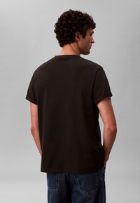 Tamnosiva majica kratkih rukava s uvrnutim rubovima, okruglim izrezom i opuštenim krojem, uparen s plavim trapericama.