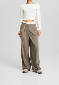 Suéter blanco cortado off-the-shoulder con textura acanalada, combinado con pantalones holgados de talle alto en color topo y zapatillas beige.