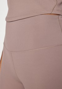 Licht mauve sportoutfit bestaande uit een aansluitende top en hoge taille leggings. Het materiaal is glad, rekbaar, met contrasterende stiksels.