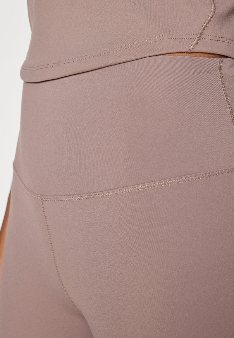 Jasnofioletowy zestaw odzieży sportowej z dopasowaną bluzką i legginsami z wysokim stanem. Materiał jest gładki, elastyczny, z kontrastowymi detalami szwów.