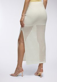 Gonna maxi in maglia color crema chiaro, con un motivo a griglia e spacco laterale. Abbinata a sandali trasparenti con tacco alto.