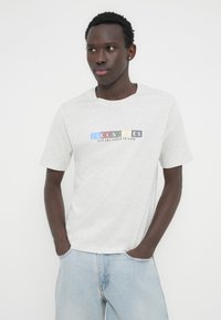 Ανοιχτό γκρι κοντομάνικο μπλουζάκι από απαλό ύφασμα, με πολύχρωμο κείμενο και το έτος ίδρυσης τυπωμένα στο στήθος.