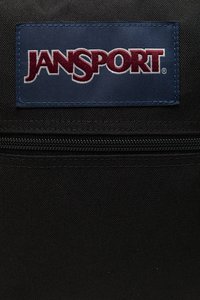 Mochila de tela negra con superficie texturizada, presenta una etiqueta rectangular azul con "JANSPORT" en texto color granate y un compartimento con cremallera.