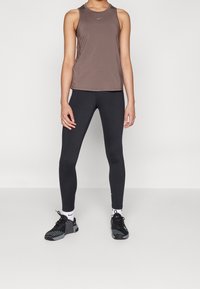Débardeur athlétique sans manches marron, leggings noirs et chaussures noires avec des accents Nike. Tissu lisse et design ajusté pour les vêtements de sport.