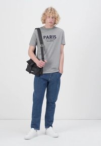Pilkas medvilnės marškinėliai su mėlynu užrašu "PARIS", derinami su mėlynomis džinsinėmis kelnėmis ir baltomis sportinėmis bateliais. Taip pat yra juoda per petį nešama rankinė.