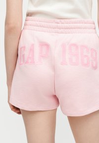Άτομο που φοράει ανοιχτό ροζ σορτς με ελαστική μέση και τη φράση «GAP 1969» κεντημένη σε πιο σκούρο ροζ στο πίσω μέρος.